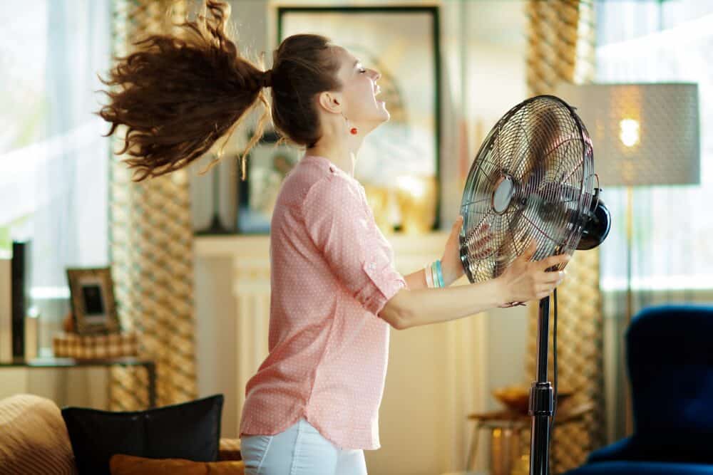 woman using a fan to her body because her AC in New Jersey home broke down